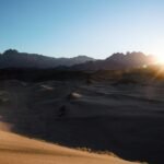 a person is walking in the desert at sunset